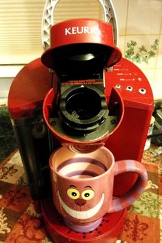 a red keurig coffee maker sitting on top of a table next to a cup