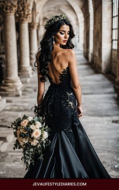 the back of a woman wearing a black dress with flowers in her hair and holding a bouquet