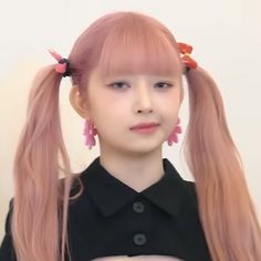 a girl with long pink hair and two ponytails is wearing black clothing, looking at the camera while standing in front of a white wall