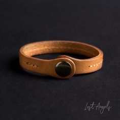 a close up of a leather bracelet on a black surface with an oval button in the middle