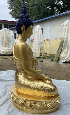 a golden buddha statue sitting on top of a white sheet in front of a building