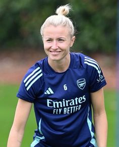 a female soccer player is smiling for the camera while sitting on the ball in front of her