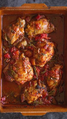 chicken with tomato sauce and herbs in a wooden dish on top of a stone table