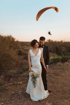 a bride and groom are standing in the desert with an orange kite flying overhead behind them