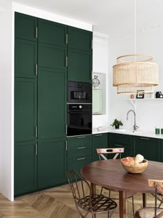 a kitchen with dark green cabinets and wooden table in front of the stove top oven