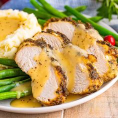 chicken breast with gravy and mashed potatoes on a plate next to green beans