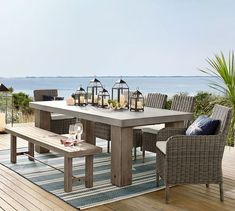 an outdoor dining table and chairs on a deck with the ocean in the back ground