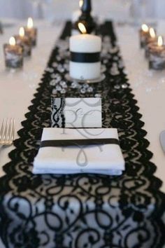 a long table with black and white place settings, silverware and candles on it