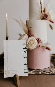 a three tiered wedding cake with flowers and feathers on the table next to it