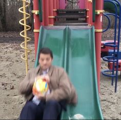 a young man sitting on top of a slide holding a ball in front of him