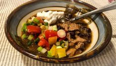 a bowl filled with meat, vegetables and sour cream on top of a tablecloth