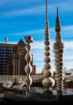 three tall sculptures in the middle of a city with buildings in the background and blue sky