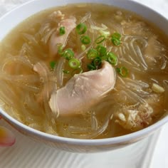 a white bowl filled with soup and meat on top of a table next to an apple