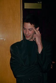 a man in a black suit talking on a cell phone while standing next to a door