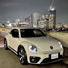 a white volkswagen beetle parked in front of a city skyline