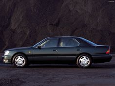 a green car is parked in front of a rock wall and black gravel area with white rims