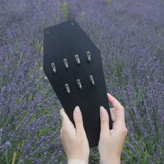 a person holding up a piece of black material in front of purple flowers and grass