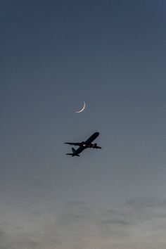 an airplane is flying in the sky at dusk with a half moon visible above it