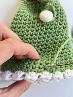 someone is crocheting a green hat with white buttons