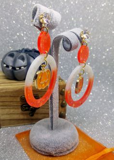 White and orange resin Halloween pumpkin earrings with holographic glitters and Jack O'Lantern charms The perfect pair of pendant earrings for Halloween night! They are entirely made in resin and glass pigments, cast in premium silicone molds. Each one of them is one of a kind since I mix resin with pigments for every single pair of earrings. Nickel-free studs with beautiful faceted crystal rhinestones and beautiful UV resin spooky Jack O'Lantern charms. Measures: approx. 7 cm (please see pictur Orange Resin Dangle Earrings, Orange Dangle Resin Earrings, Handmade Resin Jewelry For Halloween, Spooky Orange Jewelry Gift, Spooky Orange Jewelry For Gifts, Spooky Orange Halloween Jewelry, Orange Resin Jewelry For Party, Orange Resin, Pumpkin Earrings