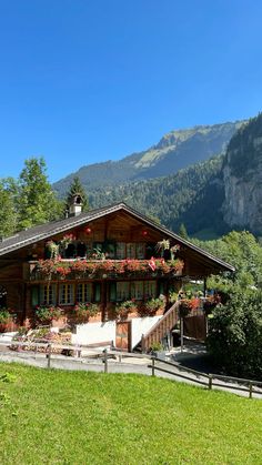 a wooden house with flowers on the balcony and mountains in the backgrouds