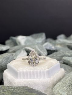 an oval shaped diamond ring sits on top of a white box with rocks in the background