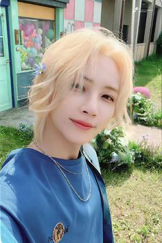 a young woman with blonde hair standing in front of a house and looking at the camera