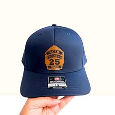 Show off your firefighter pride with our custom engraved leather patch shield hat, featuring the Fire Department Initials, Apparatus, Station Number, and Name on a  Richardson 112 hat, which is a truly unique and special accessory. Our hat is perfect for wearing on your days off or after work. The genuine leather patch is engraved with precision, adding a touch of sophistication and durability to your hat. Whether it's a gift for a firefighter, family member, coworker, friend, or even yourself, this personalized hat is a great way to show your appreciation for their hard work and dedication to the community. PRODUCT FEATURES: Patch: Genuine Leather Patch Engraving: Black Brand: Richardson 112 - Adjustable Snapback Trucker Cap Style: Structured, Six-Panel, Mid-Profile Cap Cap Material: 60% Firefighter Hat, Personalized Hat, Firefighter Family, Leather Patch Hat, Patch Hat, Firefighter Gifts, Cap Style, Hard Work And Dedication, Fire Dept