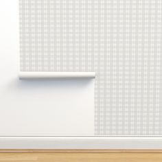 an empty room with a white wall and wood flooring next to a shelf that has a rolled up piece of paper on it