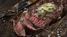 a steak is sitting on a wooden table next to a knife and fork