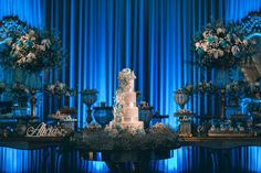 a white wedding cake sitting on top of a table with blue drapes behind it