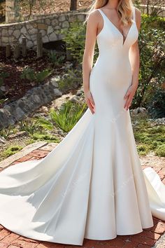 a woman wearing a white wedding dress standing on a brick walkway in front of trees