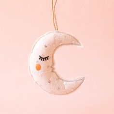 Photo is a felted moon ornament hanging on a jute piece of string.  The moon is white with black eyelashes and an orange circle cheek.  The moon also has silver sequins sewn onto it. Handmade Star Ornaments, Felt Moon Ornaments, Sun Felt Ornament, Moon Felt Ornament, Moon Ornament, Felted Wool Crafts, Sweets Gift, Night Moon, Felt Ornament