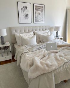 a laptop computer sitting on top of a bed covered in white blankets and pillows next to two framed pictures