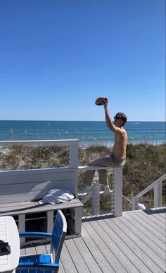 a man sitting on top of a wooden deck next to the ocean with his arm in the air