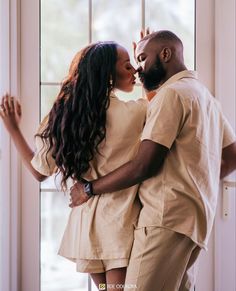 a man and woman standing next to each other near a window with their arms around each other