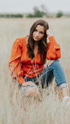 a woman sitting in the middle of a field with her hands on her head and looking at the camera