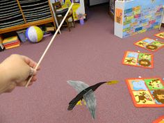 a person is holding a stick and playing with animals on the floor in front of children's bookshelves