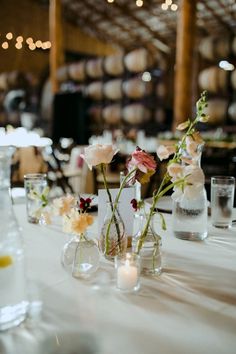 the table is set with vases and flowers on it, along with empty wine glasses