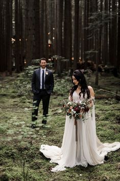 a bride and groom standing in the woods