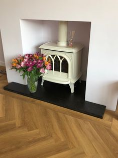 a vase with flowers sitting on top of a wooden floor next to a stove in a room