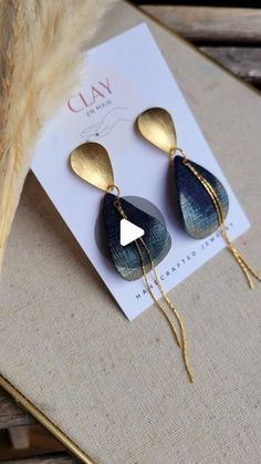 two pairs of gold and blue earrings on top of a piece of paper next to a feather