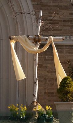 a cross with white drapes hanging from it's sides in front of a building