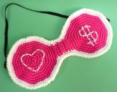 a pink and white crocheted object with hearts on it's side, sitting on a green surface