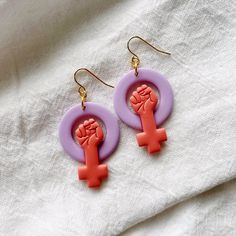 two pairs of pink and purple earrings with an orange fist on the front, one in the middle