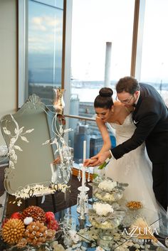 a bride and groom cutting their wedding cake at the top of a table in front of a large window