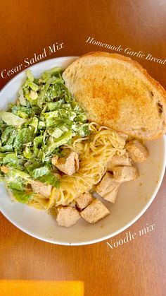 a white plate topped with pasta and meat next to a sandwich on top of a wooden table