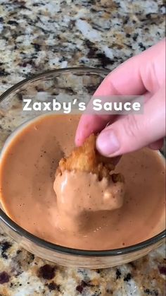 someone dipping something into a glass bowl on top of a marble counter with the words zaxby's sauce over it