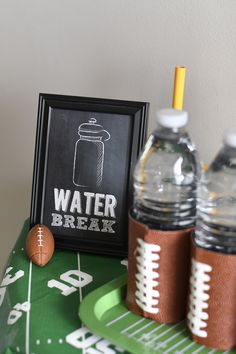 a table topped with water bottles and footballs next to a framed sign that says water break