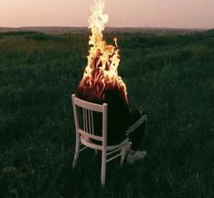 a person sitting in a white chair on top of a field next to a fire